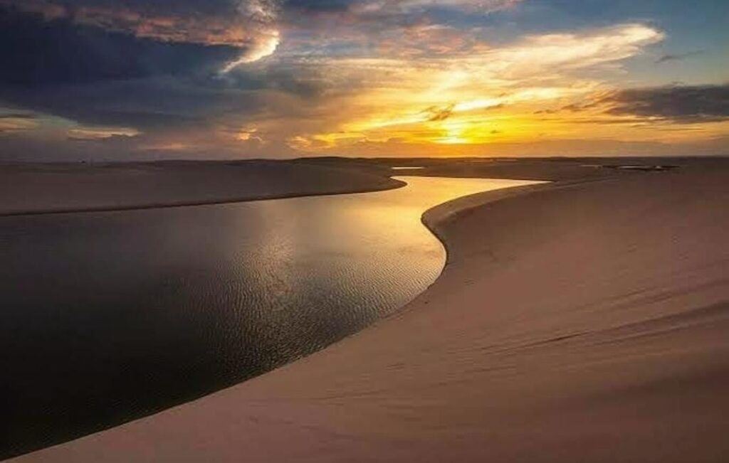 Pôr do sol dourado sobre lagoa e dunas nos Lençóis Maranhenses