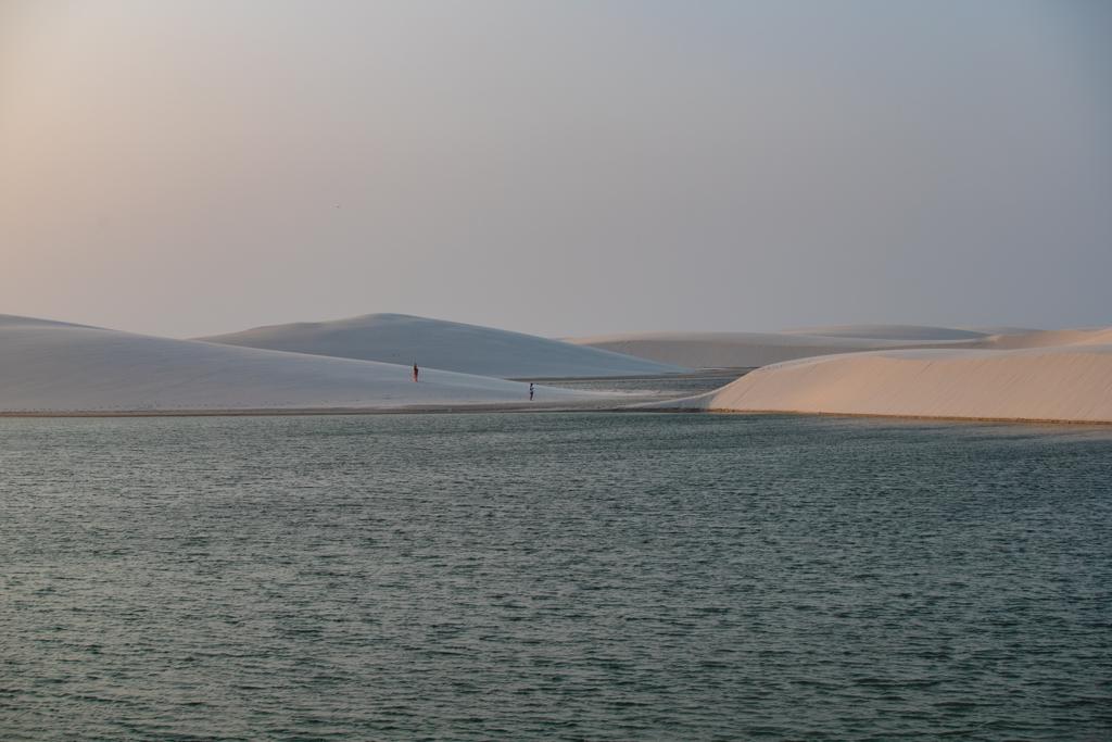 Lagoa com pessoas caminhando nas dunas ao entardecer nos Lençóis Maranhenses